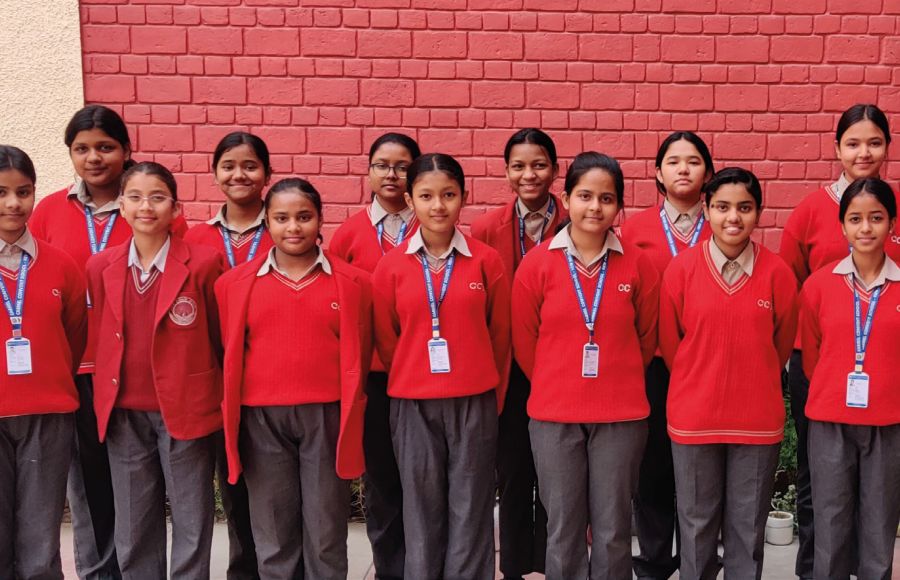 Die Stipendiatinnen der Carmel Convent School aus dem Jahrgang 2024 stehen in rot-schwarzer Schuluniform vor einer rot gestrichenen Wand.