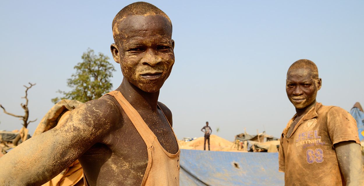 Zwei Männer aus einer Goldmine in Burkina Faso blicken in die Kamera. Ihre Haut und ihre Hemden sind von der Arbeit verschmutzt.