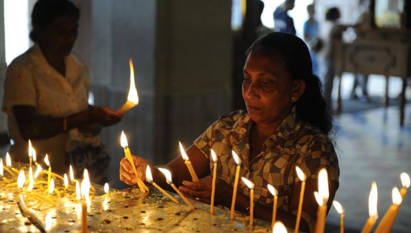 Eine Frau zündet in einer dunklen Kirche Kerzen an.