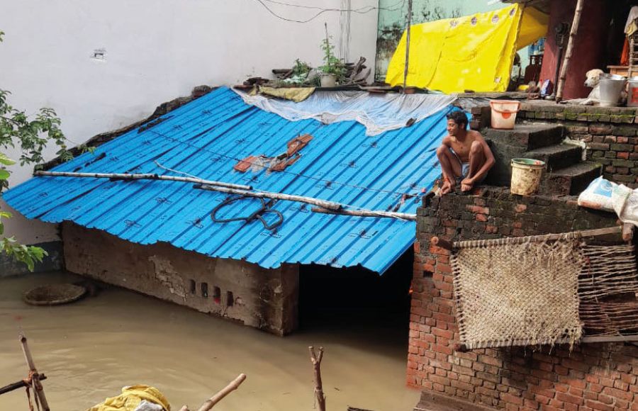 Flut in Indien: Ein Mann sitzt erhöht auf einer Mauer neben einer Wellblechhütte, die zu großen Teilen bereits überschwemmt ist.