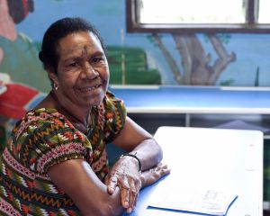 Eine erwachsene Frau sitzt in einer Schulbank in Papua-Neuguinea und lächelt in die Kamera.