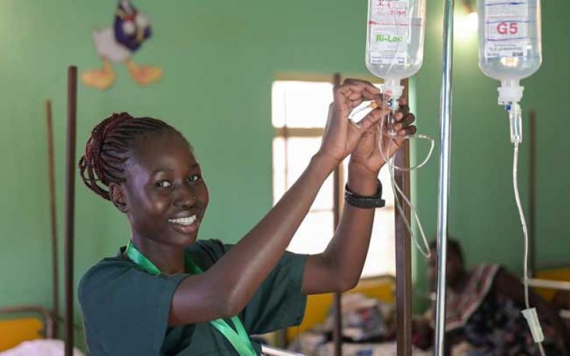 Eine junge Krankenschwester aus dem Südsudan schließt eine Infusionskanüle an und lacht in die Kamera.