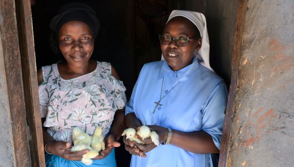 Schwester Veronica aus Uganda steht mit einer Frau im Türrahmen. Beide haben Küken in ihren Händen.