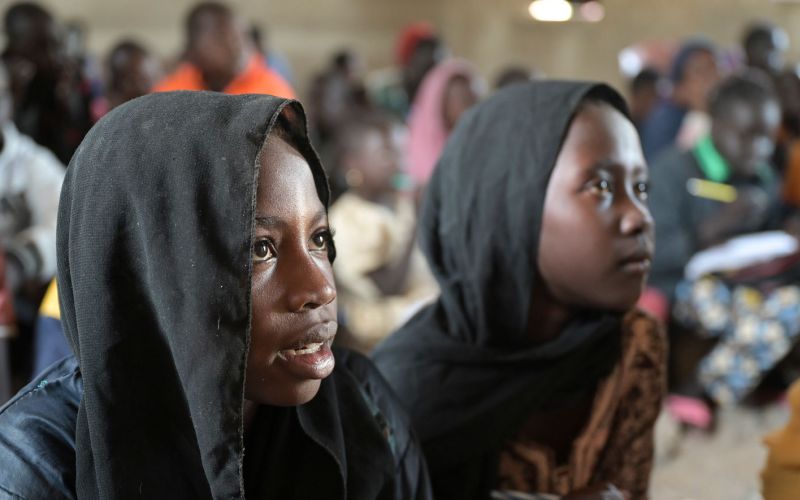 Zwei Mädchen mit schwarzen Kopftüchern blicken in einem improvisierten Unterrichtsraum in einem Flüchtlingscamp im Südsudan zur Tafel