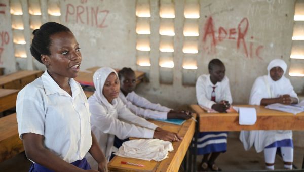 Schülerinnen an der Blue State Secondary des JRS in Kenia sitzen in einem Klassenzimmer. Ein Mädchen im Vordergrund steht und spricht in Richtung Tafel nach vorne.