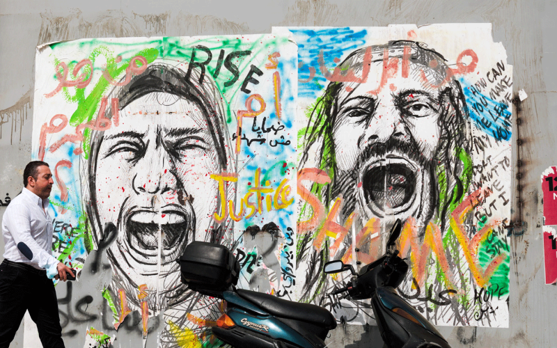 Ein Mann geht auf einer Straße in Beirut an bemalten Wänden vorbei. Die Graffiti zeigen schreiende Menschen - Symbolbild für die Notlage im Libanon