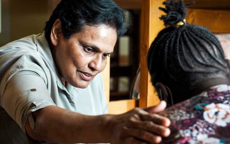 Eine Ordensschwester legt tröstend den Arm auf die Schulter einer jungen Frau, die im Bild nur von hinten zu sehen ist.