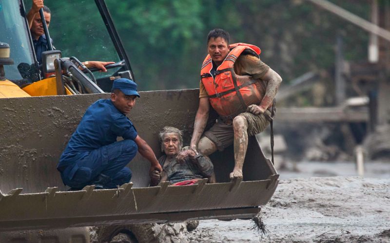 Nepal: Eine alte Frau sitzt erschöpft in einer Baggerschaufel, neben ihr zwei Retter