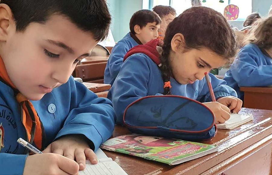 Kinder sitzen in Schulbänken und schreiben