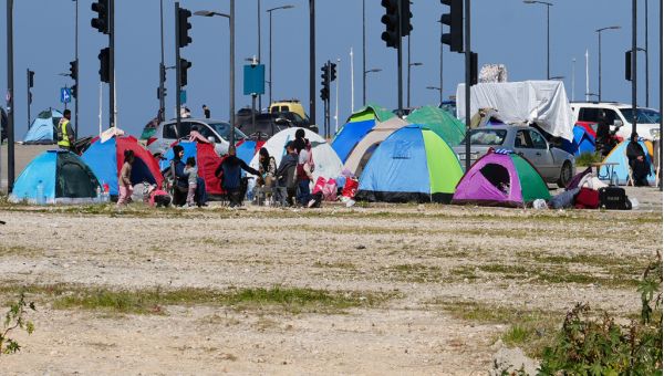 Bunte Zelte stehen auf einem sandigen, kärglich bewachsenen Platz. Im Hintergrund zahlreiche Ampeln und der strahlend blaue Himmel.