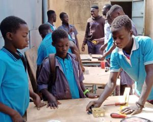 Jugendliche in Burkina Faso erlernen ein Handwerk: im Vordergrund stehen drei Jugendliche in hellblauen T-Shirts an einer Werkbank.