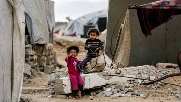 Zwei Kinder sitzen in einem Flüchtlingslager in Gaza auf den Trümmern eines Hauses.