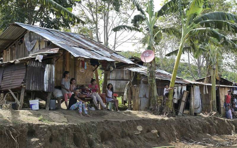 Menschen sitzen auf der philippinischen Insel Mindanao vor ihren ärmlichen mit Wellblech bedeckten Behausungen. Dazwischen wachsen Palmen.