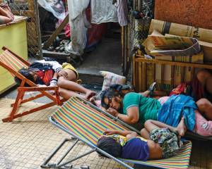 Eine Frau schläft mit ihren Kindern am Rand einer Straße in Manila auf einem Bretterverschlag. Zwei Kinder schlafen auf Klappstühlen.