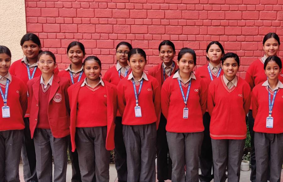 Die Stipendiatinnen der Carmel Convent School aus dem Jahrgang 2024 stehen in rot-schwarzer Schuluniform vor einer rot gestrichenen Wand.