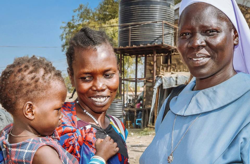 Afrikatag 2026: Eine Schwester aus Südsudan steht bei einer Frau, die ein Kind auf dem Arm hält.
