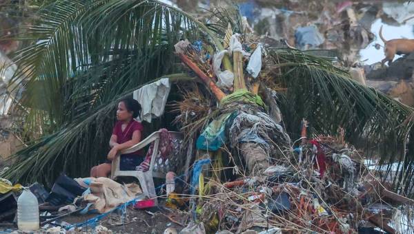 Nach dem verheerenden Taifun Kalmaegi auf der philippinischen Insel Cebu sitzt eine Frau in einem Plastikstuhl unter den Blättern einer umgestürzten Palme. Um sie herum Trümmer, Geröll, Kleiderfetzen und Chaos.