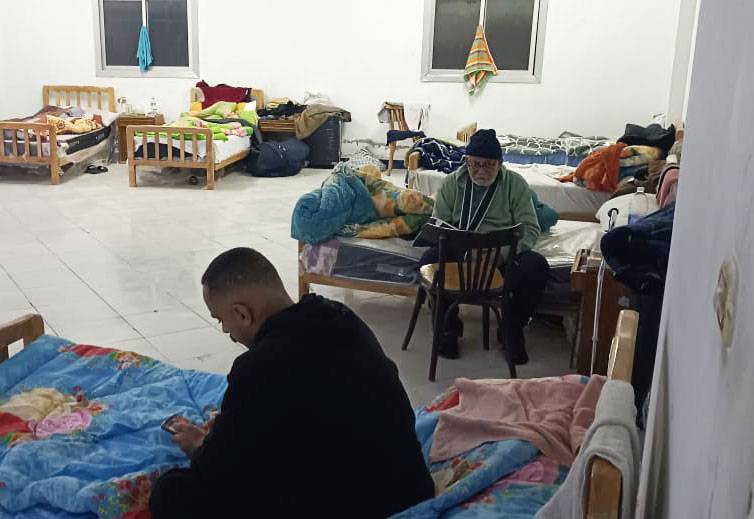 Blick in einen Schlafsaal mit Geflüchteten aus Gaza. Sie sind in Ägypten untergekommen. Zwei Männer, einer alt, einer jung, lesen auf ihren Betten.