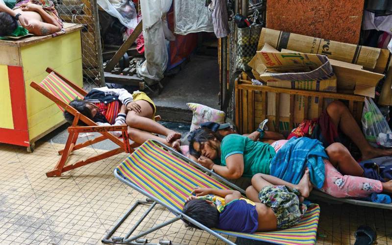 Eine Frau schläft mit ihren Kindern am Rand einer Straße in Manila auf einem Bretterverschlag. Zwei Kinder schlafen auf Klappstühlen.