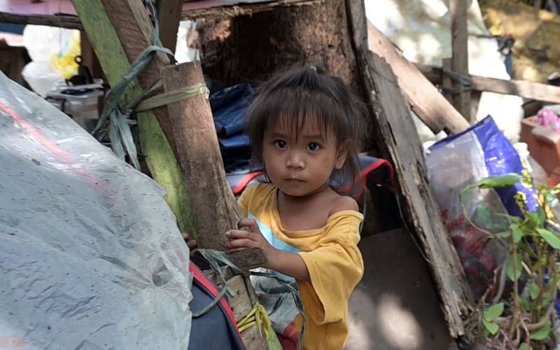 Ein philippinisches Kind blickt vorsichtig aus einem Holzverschlag