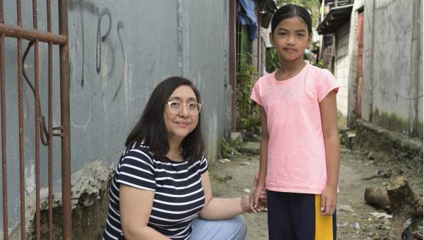 Projektpartnerin Carol Daria hat ein Mädchen an der Hand, das seinen Vater verloren hat. Sie stehen in einer heruntergekommenen Gasse in Payatas, Philippinen