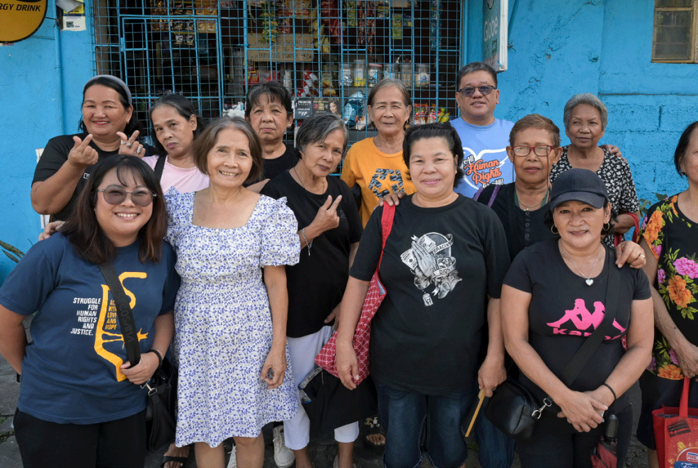Father Toots steht mit einer Gruppe von Frauen vor einem geschossenen kleinen Geschäft. Die Frauen sind Angehörige der Opfer von Dutertes Krieg gegen die Drogen. Foto: Jörg Böthling