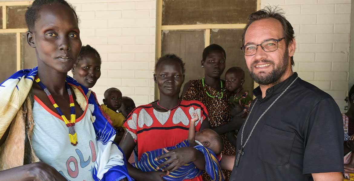 Zu sehen ist eine Gruppe von Menschen aus dem Südsudan, rechts vorne im Bild steht missio-Projektpartner Christian Carlassare, Bischof von Bentiu.