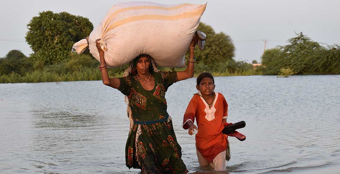 Eine Frau geht mit ihrem Kind durch überflutetes Gebiet in Pakistan.