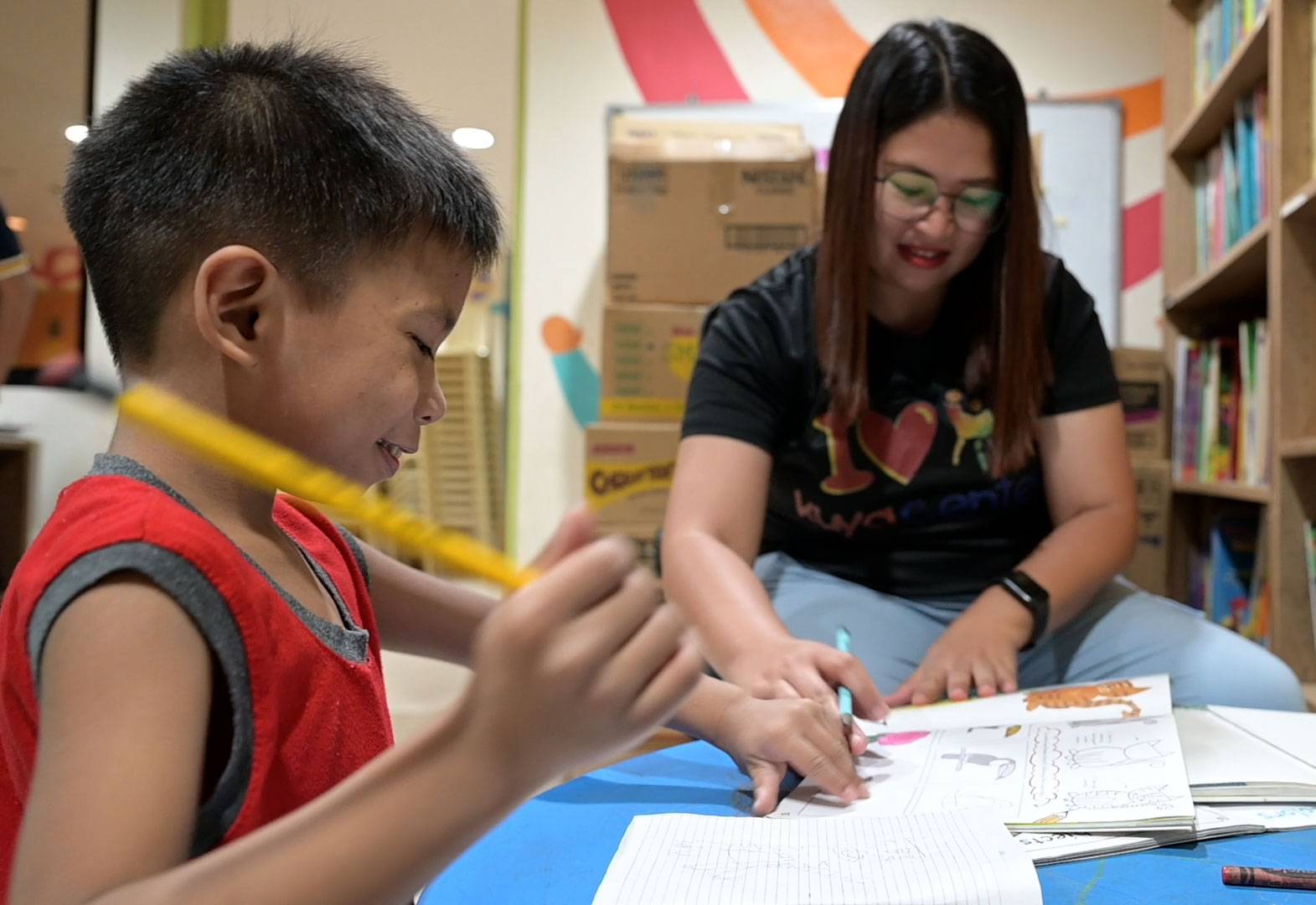 Ein Junge und eine Betreuerin sitzen über Schulheften
