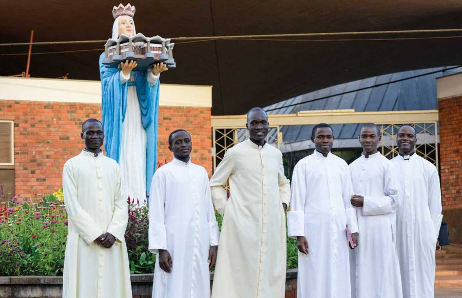 Gruppenfoto von sechs Priesteramtskandidaten in Uganda, alle in weiß gekleidet.