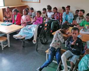 Rund 20 Kinder aus Äthiopien sitzen in einem Klassenraum an Tischen und dazwischen und blicken nach vorne Richtung Kamera.