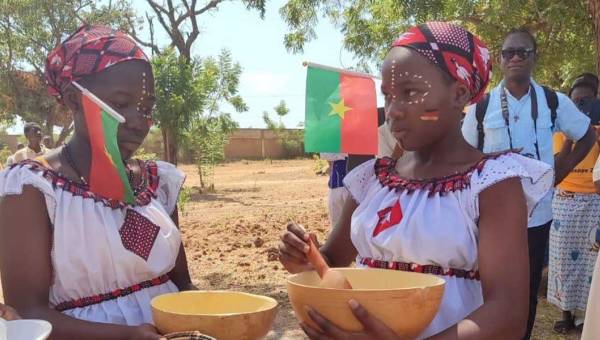 Zwei junge Frauen aus Burkina Faso haben zwei Holzschüsseln in der Hand und sind geschmückt mit burkinischen und deutschen Flaggen.