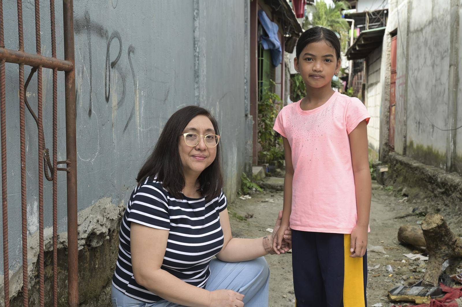 Unsere Projektpartnerin Carol Daria kniet neben Yessa in einer Gasse in Payatas im Großraum Manila