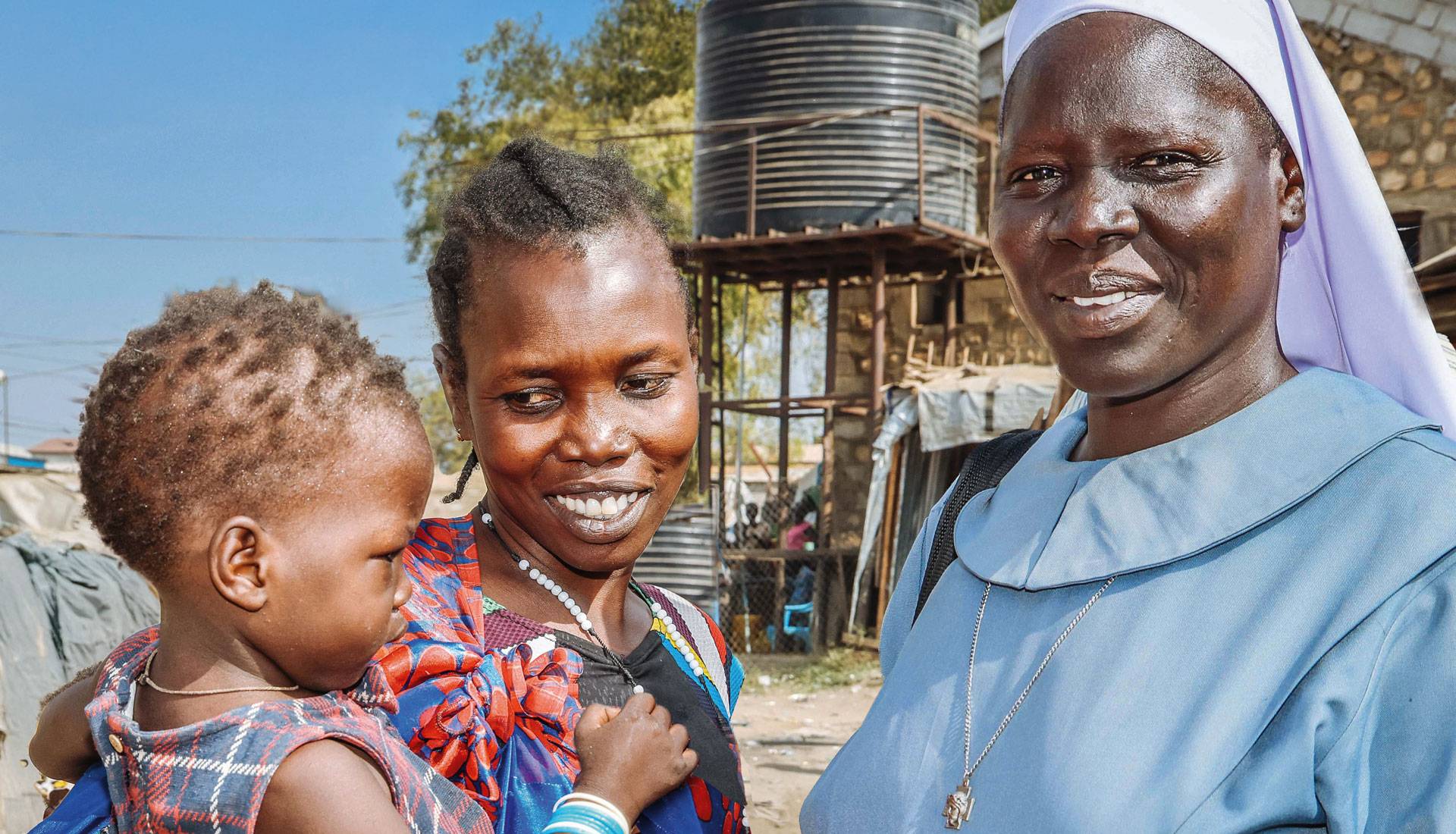 Afrikatag 2026: Eine Schwester aus Südsudan steht bei einer Frau, die ein Kind auf dem Arm hält.